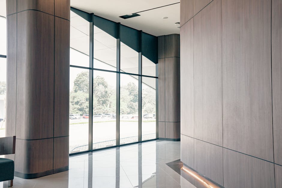 Spacious modern lobby featuring large windows, wooden panels, and a reflective floor creating a serene atmosphere.